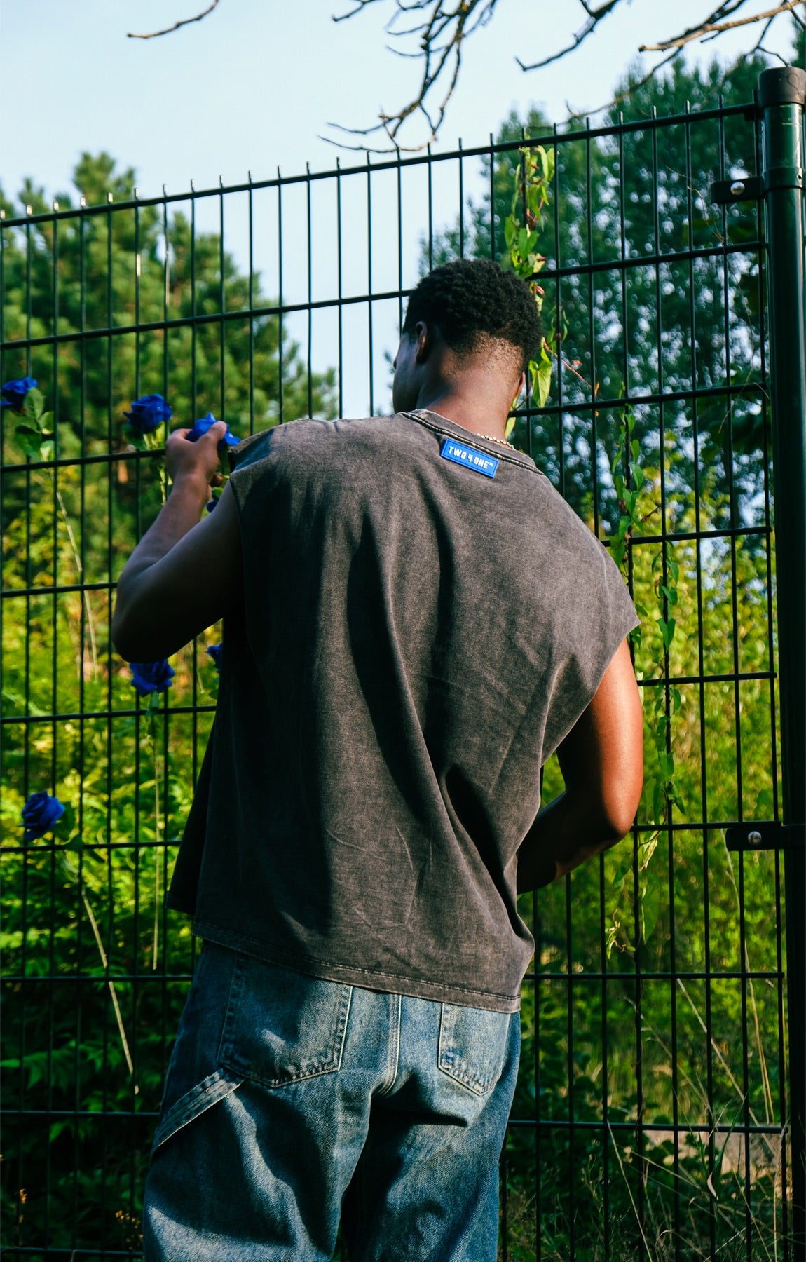 Rug van een model bij een groen hek met blauwe rozen